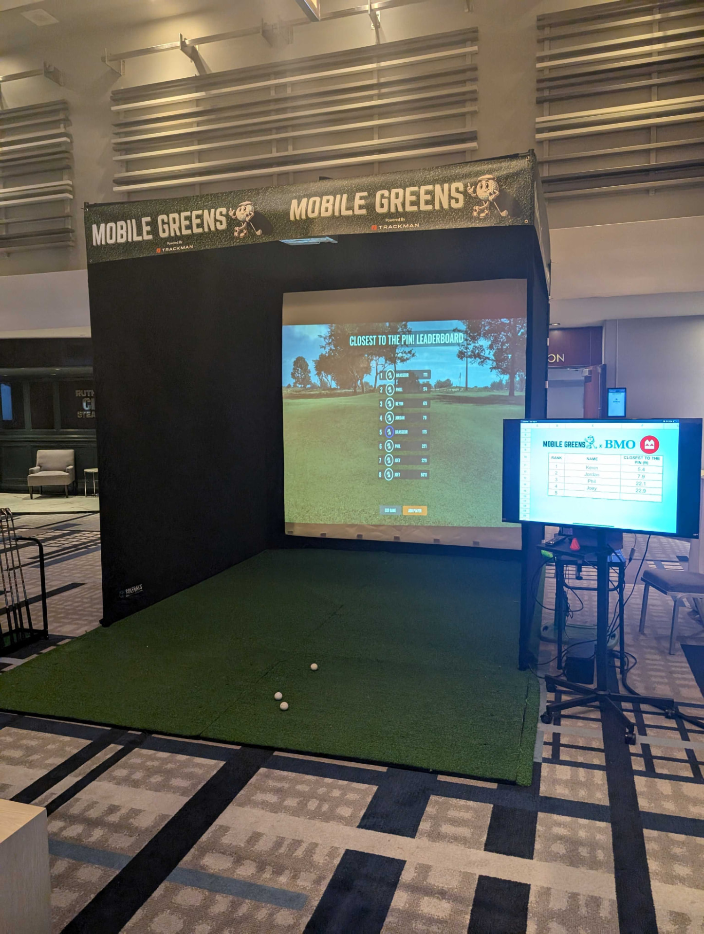 Mobile Greens simulator bay with BMO branded leaderboard at an indoor corporate event
